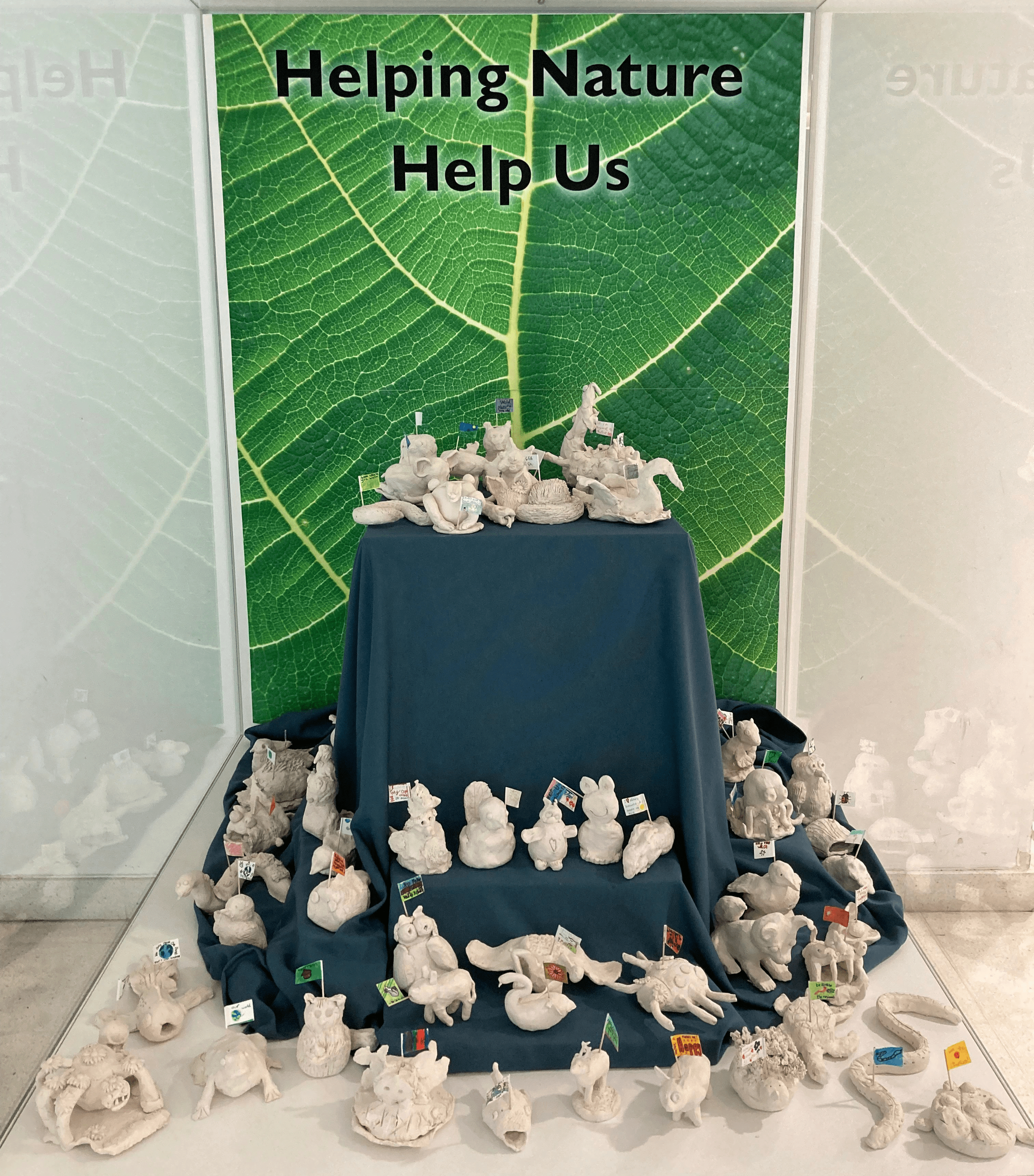 Display of clay sculptures created by school pupils in front of a green close up image of a leaf